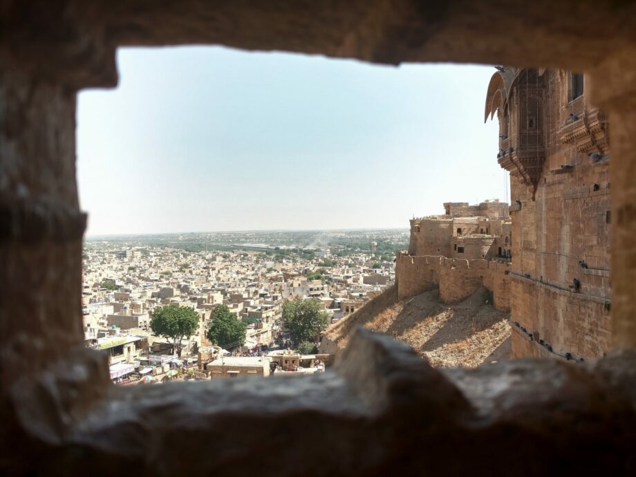 Ausblick durch ein Bruchsteinfenster einer alten Burg auf eine indische Stadt mit Flachdachhäusern.