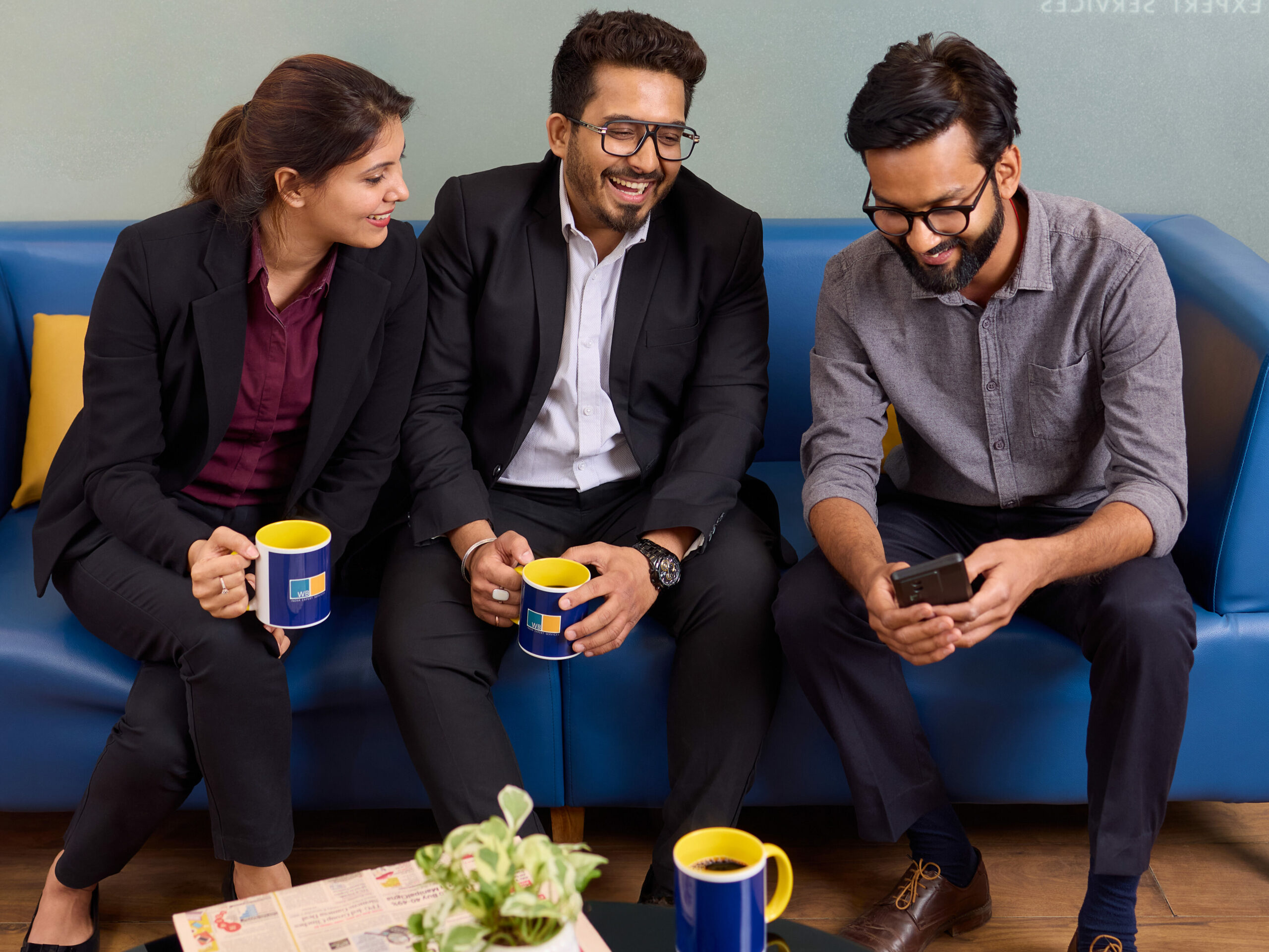 Gelöste Pausensituation im Wamser + Batra HQ Delhi. Eine Mitarbeiterin schaut gemeinsam mit zwei anderen Kollegen auf einem Sofa sitzend in ein Smartphone.