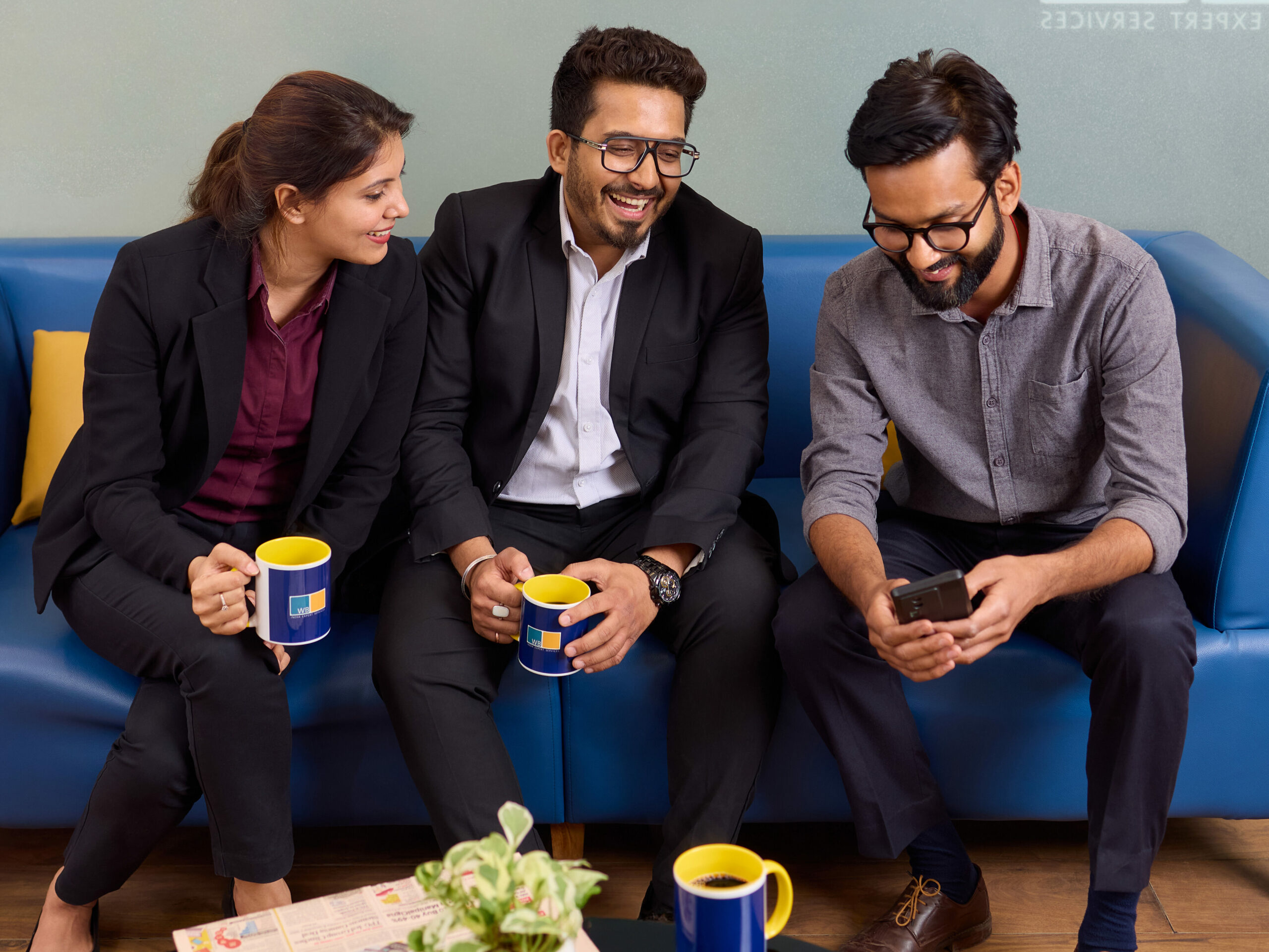 Eine Kollegin und zwei Kollegen des indischen Wamser + Batra Teams schauen gemeinsam in ein Smartphone.