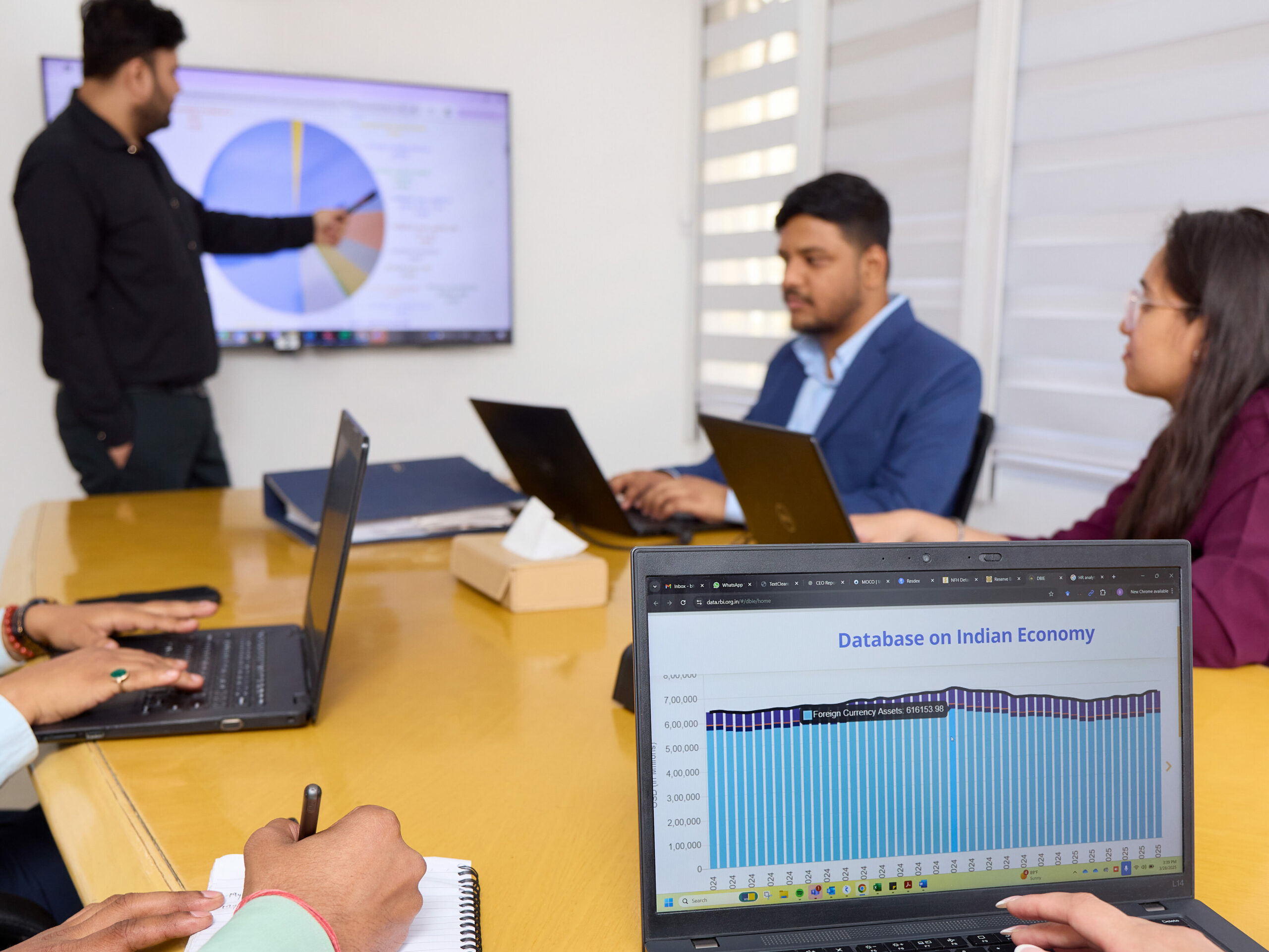 Ein Mitarbeiter erläutert einem Team am Flipchart ein Kreisdiagramm während eines Meetings zum indischen Wirtschaftswachstum.