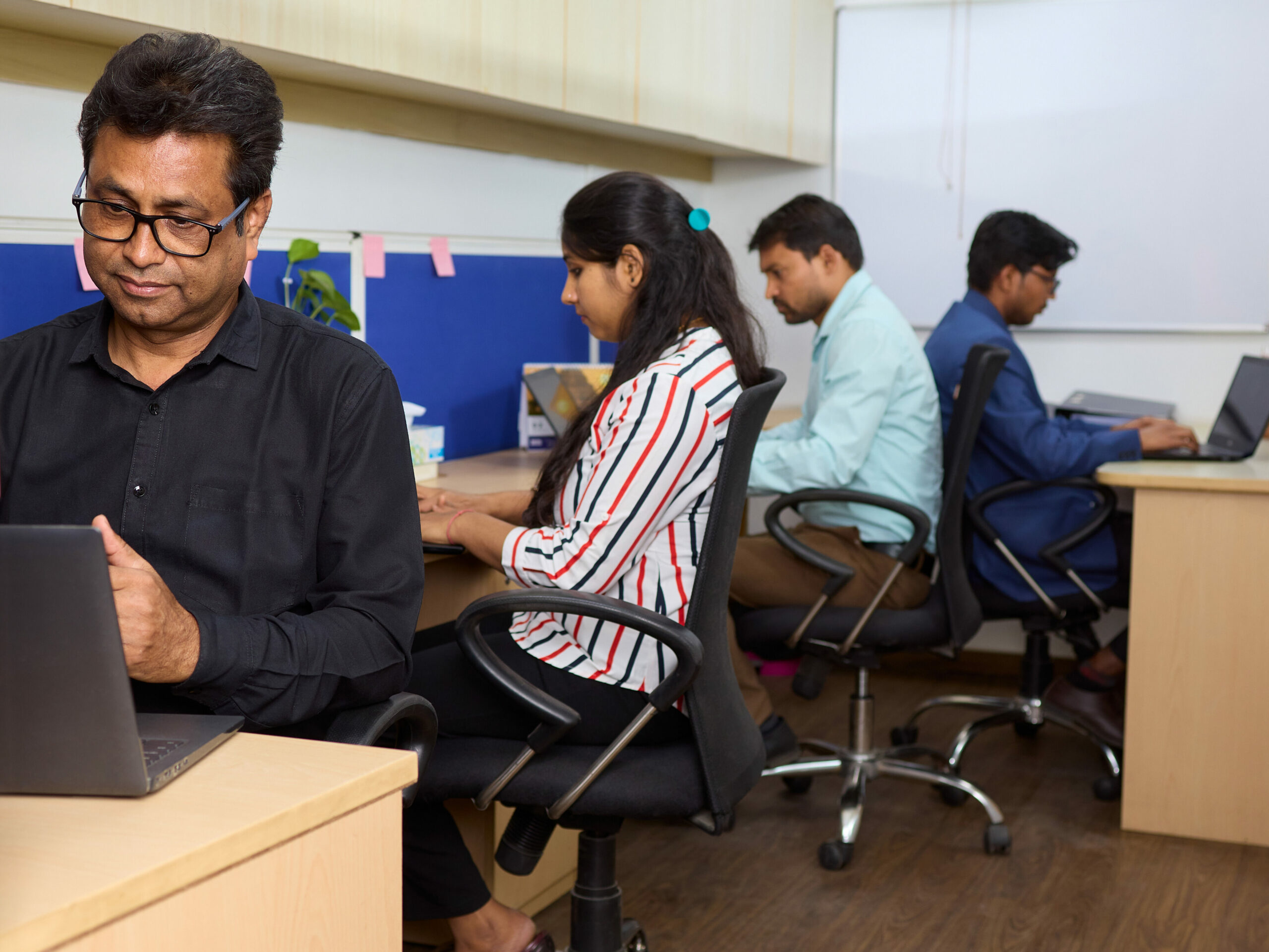 Großraumbüro des Wamser + Batra HQ Delhi. Eine Mitarbeiterin und drei Mitarbeiter sitzen an ihren Schreibtischen und arbeiten am Laptop.