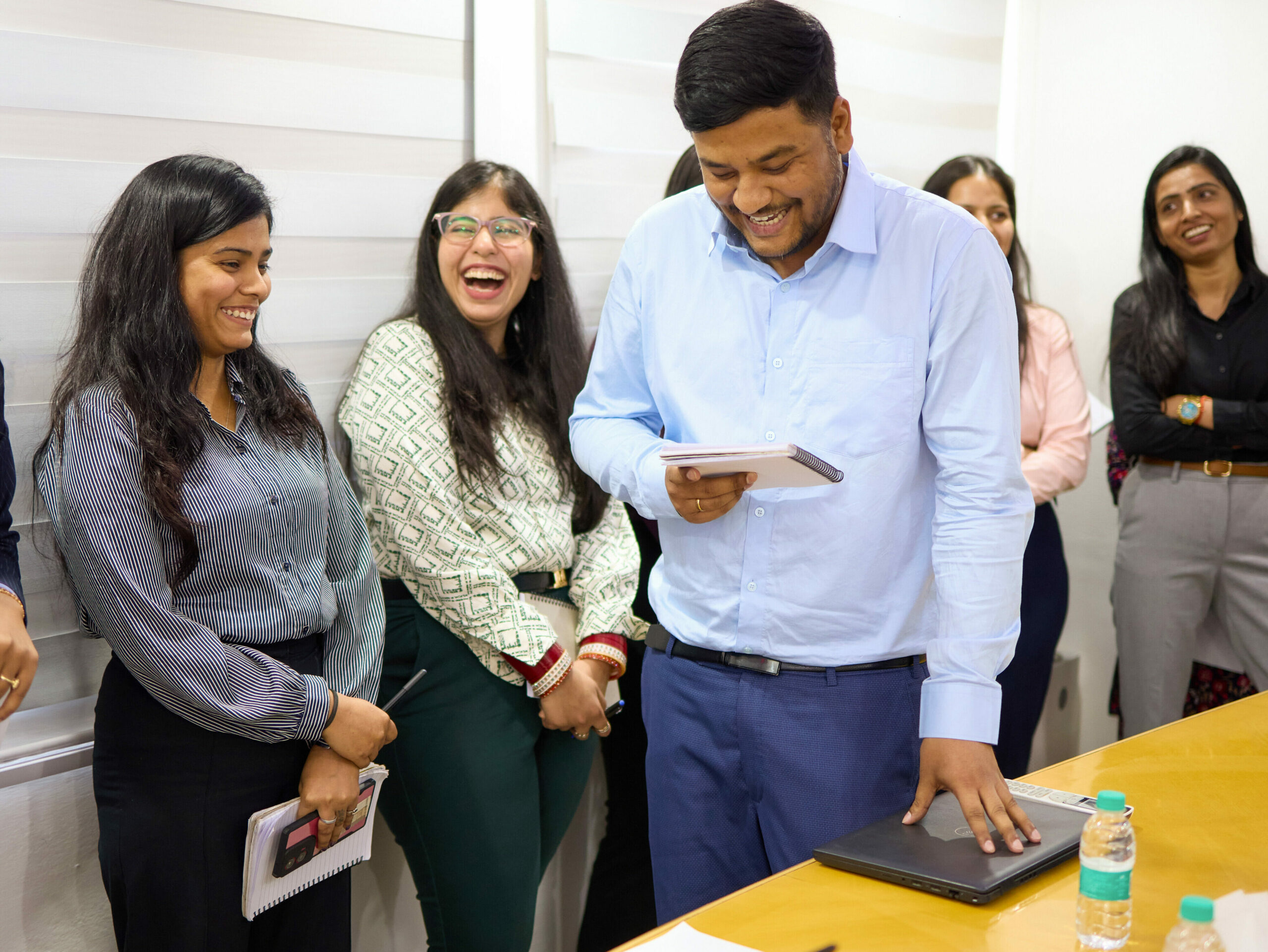 Gelöste Arbeitssituation im Wamser + Batra HQ Delhi. Ein Mitarbeiter schaut in seine Notizen, während fünf Kolleginnen sich miteinander lachend unterhalten.